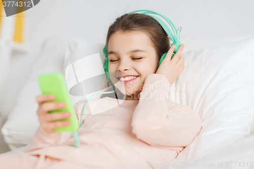 Image of happy girl lying in bed with smartphone at home