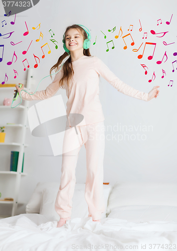 Image of girl jumping on bed with smartphone and headphones