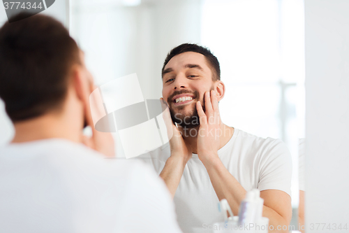 Image of happy young man looking to mirror at home bathroom