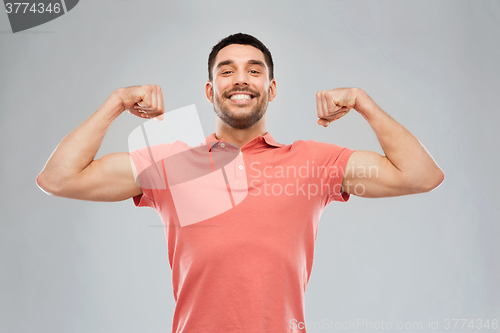 Image of smiling man showing biceps over gray background