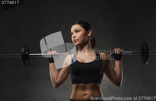 Image of young woman flexing muscles with barbell in gym