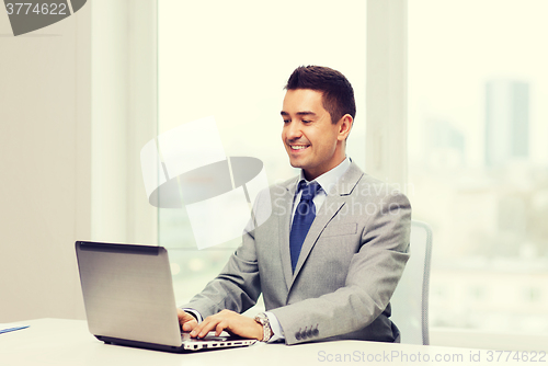 Image of happy businessman working with laptop in office