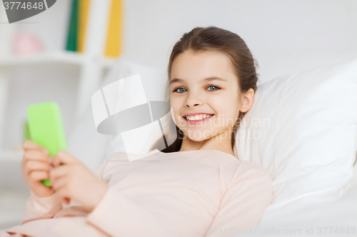 Image of happy girl lying in bed with smartphone at home