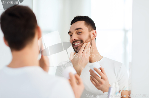 Image of happy young man applying cream to face at bathroom