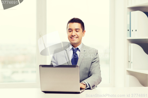 Image of happy businessman working with laptop in office