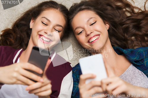 Image of happy teenage girls lying on floor with smartphone