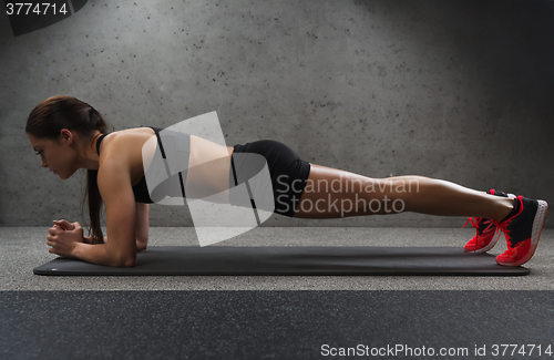 Image of woman doing plank exercise on mat in gym