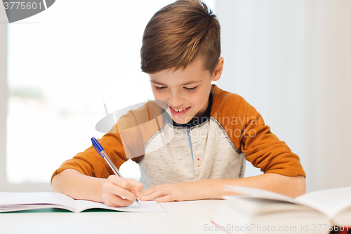 Image of smiling student boy writing to notebook at home