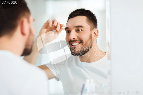 Image of man with tweezers tweezing eyebrow at bathroom