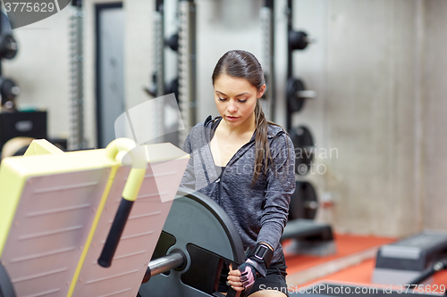 Image of young woman adjusting leg press machine in gym