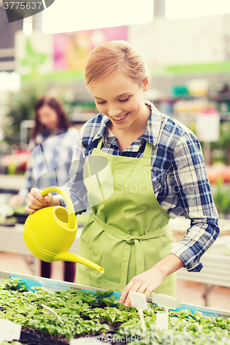 Image of happy woman with watering can in greenhouse