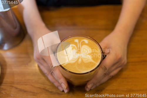 Image of close up of hands with latte art in coffee cup