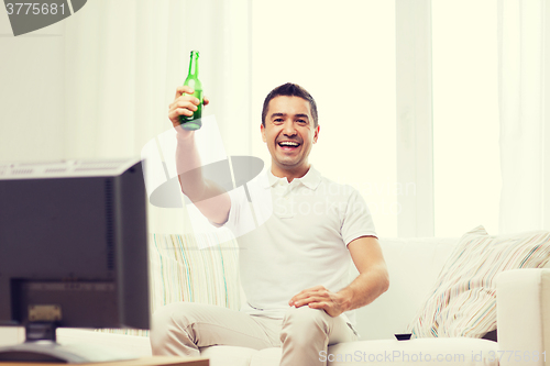 Image of smiling man watching tv and drinking beer at home