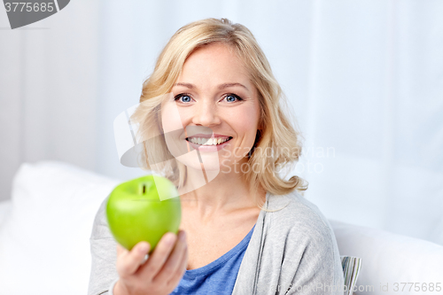 Image of happy middle aged woman with green apple at home