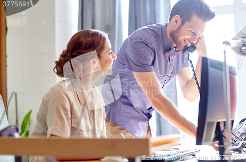 Image of happy creative team calling on phone in office