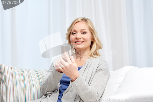 Image of smiling woman with smartphone texting at home