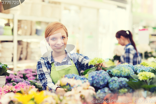 Image of happy woman taking care of flowers in greenhouse