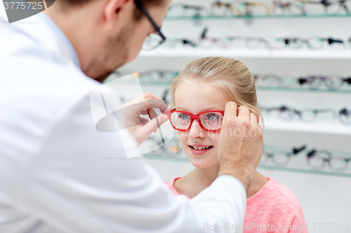 Image of optician putting glasses to girl at optics store
