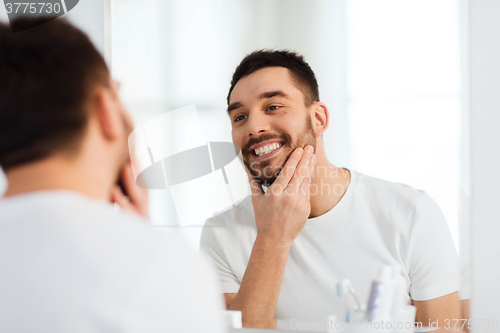 Image of happy young man looking to mirror at home bathroom