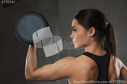 Image of young woman flexing muscles with dumbbells in gym