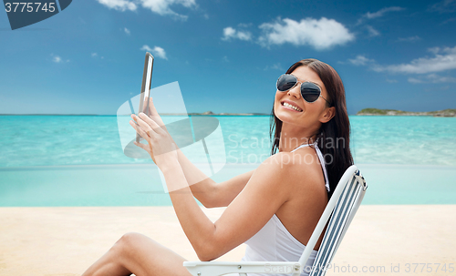 Image of smiling woman with tablet pc sunbathing on beach