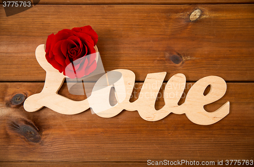 Image of close up of word love cutout with red rose on wood