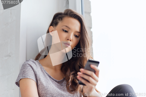 Image of sad pretty teenage girl with smartphone texting