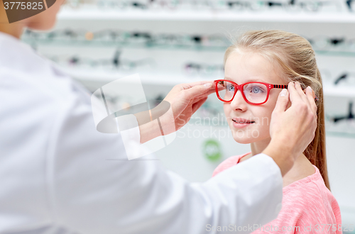 Image of optician putting glasses to girl at optics store