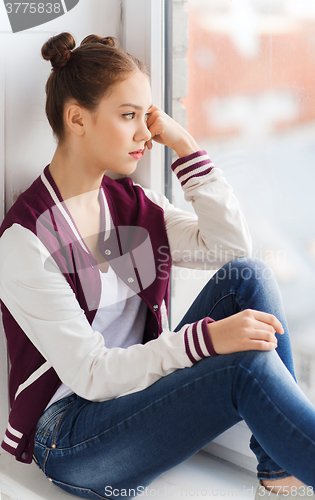 Image of sad pretty teenage girl sitting on windowsill