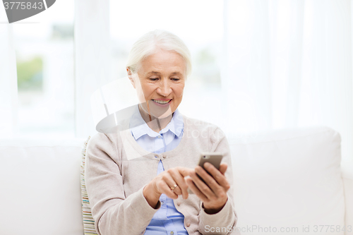 Image of senior woman with smartphone texting at home