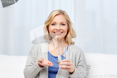 Image of happy woman with medicine and water glass at home