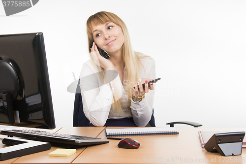 Image of Happy secretary looked at the computer screen talking on the phone working and holding a cell