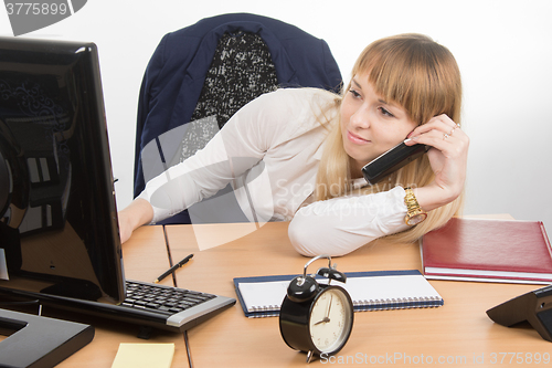 Image of Tired office employee lying on the desk talking on the phone and looked at the screen