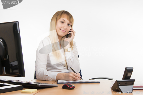 Image of Happy business woman talking on a mobile phone writing in a diary