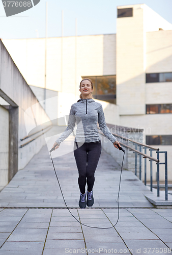 Image of happy woman exercising with jump-rope outdoors