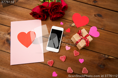 Image of close up of smartphone, gift, red roses and hearts