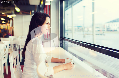 Image of smiling young woman drinking coffee at cafe