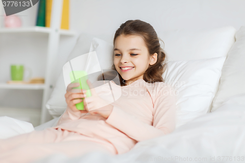 Image of happy girl lying in bed with smartphone at home