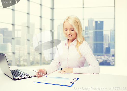 Image of smiling businesswoman reading papers in office