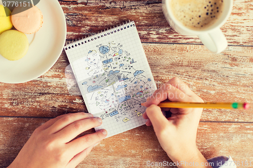 Image of close up of hands drawing scheme to notebook
