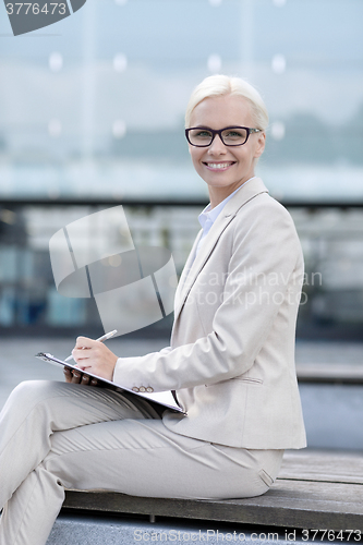 Image of young smiling businesswoman with notepad outdoors