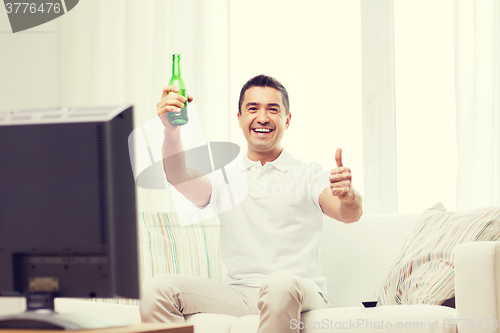 Image of smiling man watching tv and drinking beer at home