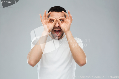 Image of man making finger glasses over gray background