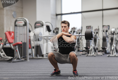 Image of young man flexing muscles with barbell in gym