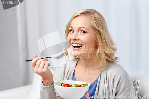 Image of smiling middle aged woman eating salad at home