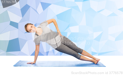 Image of woman making yoga in side plank pose on mat