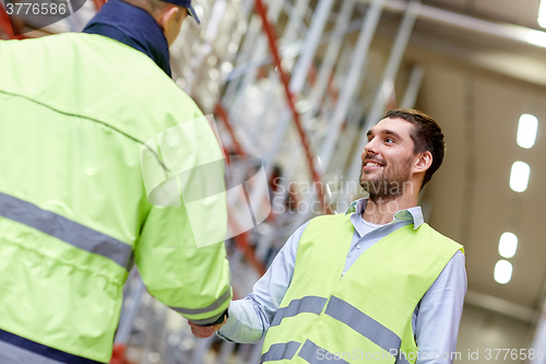 Image of men in safety vests shaking hands at warehouse