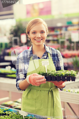 Image of happy woman holding seedling in greenhouse