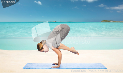 Image of woman making yoga in crane pose on mat over beach 