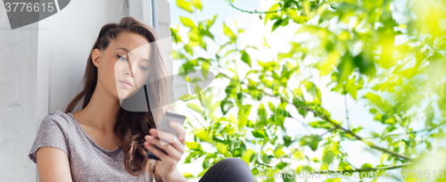 Image of sad pretty teenage girl with smartphone texting